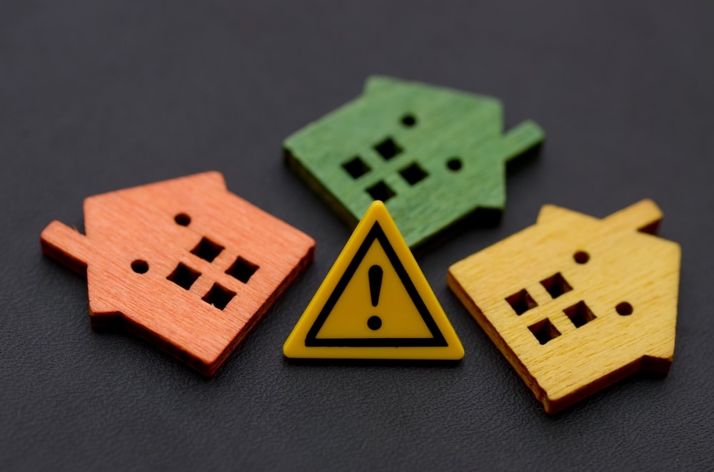 ThreeMiniatureHousesWithWarningExclamationSign—RealEstate